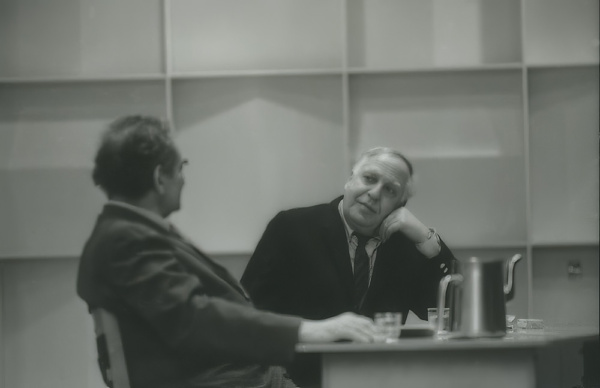 Black-and-white photo of two men, Harold Rosenberg and Philip Guston, in conversation at separate desks.